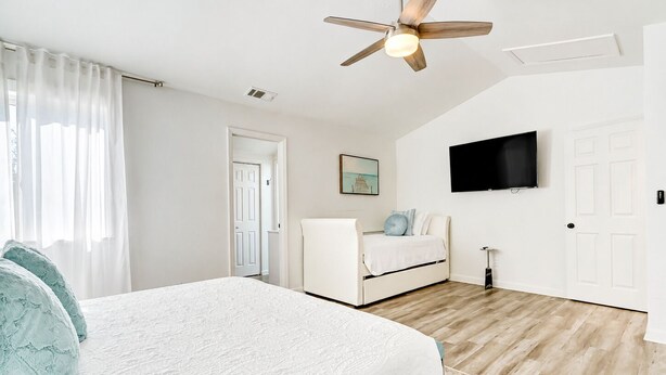 Une chambre à coucher avec un lit, un ventilateur de plafond, une télévision et une porte.