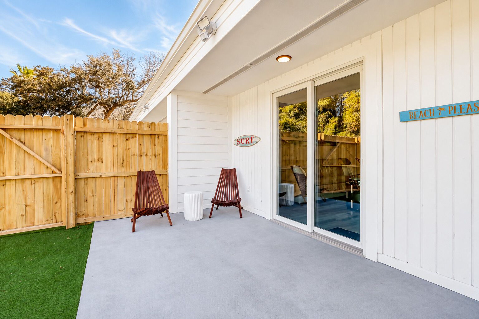 A covered patio area with two wooden chairs, a wooden fence, and a sign that reads 'BEACH PLEASE SURF'.