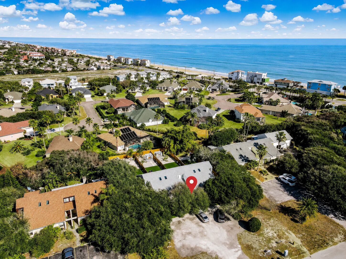 Vue aérienne d’un quartier résidentiel avec des maisons, des routes et une plage en arrière-plan.