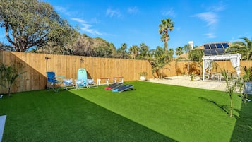 Un jardin avec une pelouse artificielle, une clôture en bois, des palmiers et une pergola blanche.
