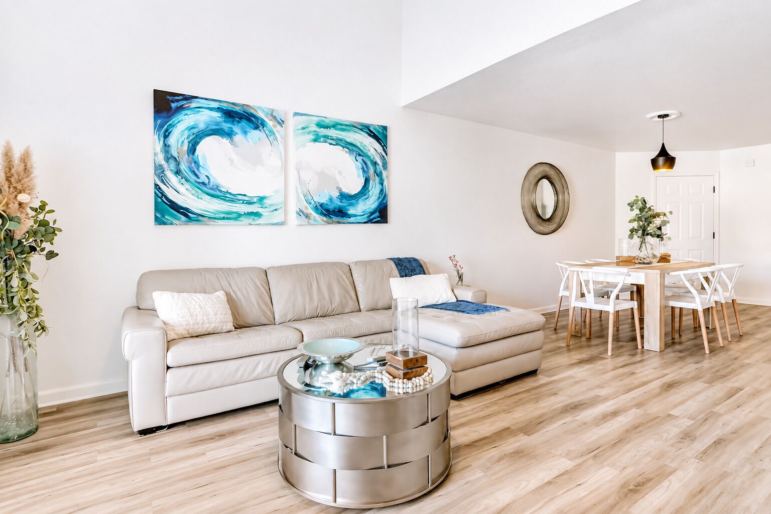 Un salon avec un canapé beige, une table basse ronde et un coin repas comprenant une table et des chaises blanches.