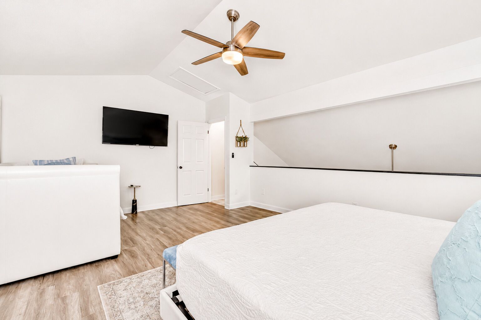 Une chambre moderne avec un lit, un téléviseur, un ventilateur de plafond et un plancher en bois.