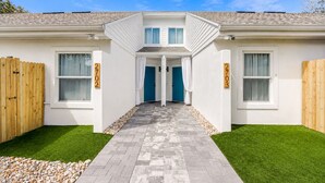 Une maison à deux étages avec une allée dallée, une porte bleue et le numéro « 2703 » peint sur le mur.