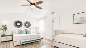 Une chambre à coucher avec un lit, des tables de chevet, un banc, un ventilateur de plafond et un tableau au mur.