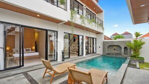 Una casa moderna de dos pisos con piscina, ventanas amplias y mobiliario de exterior.
