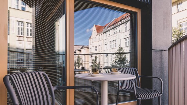 Een balkon met twee stoelen en een kleine ronde tafel, met uitzicht op een stadsgezicht met klassieke gebouwen.