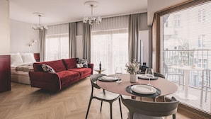 Een moderne woonkamer met een rode bank, een eettafel gedekt voor twee personen en een groot raam met zonwering.