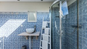 Un baño con lavamanos blanco, un espejo, toallero y ducha con mosaicos azules.