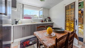 Una cocina con una mesa de comedor, sillas, un refrigerador, un microondas y una ventana.