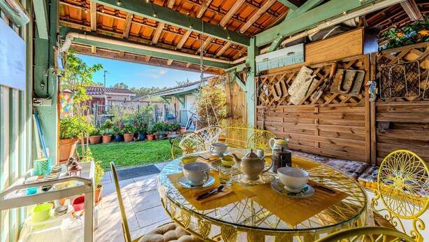 Un patio al aire libre con una mesa redonda de vidrio, sillas amarillas y una pared de madera con un diseño de celosía.