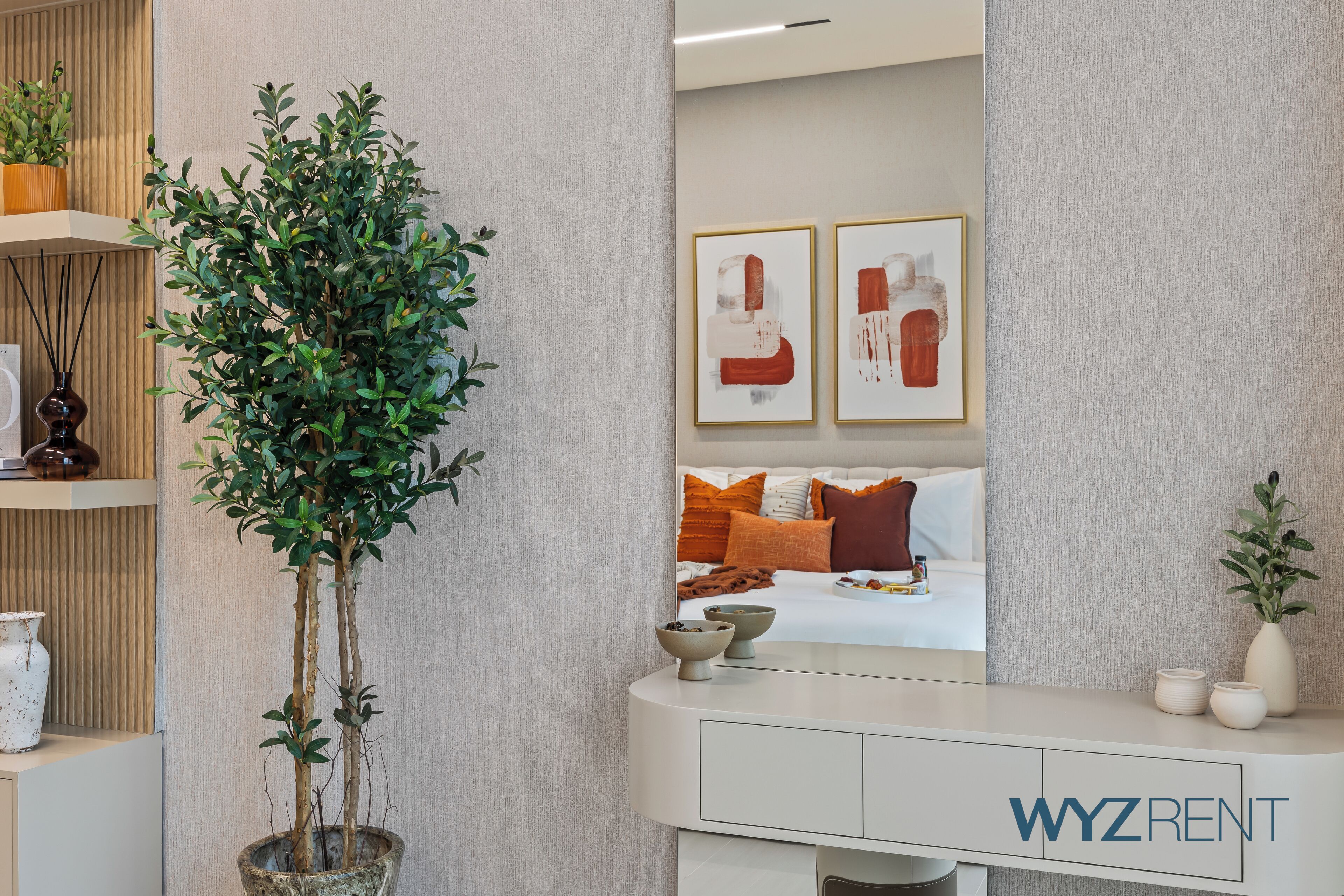A modern hotel room with a large potted plant, a white console table, and artwork on the wall.