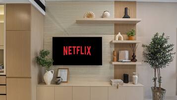 A modern living room with a mounted TV displaying "NETFLIX" in red letters, wooden cabinets, a potted plant, and decorative items on shelves.