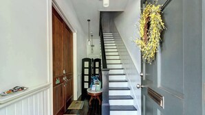 A hallway with a wooden door, a staircase, and a door with a wreath. - The Whale Loft | Historic Charm + Balcony (Savannah)