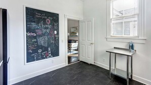 A hallway with a chalkboard wall, a door leading to a storage area, and a window with blinds. - The Whale Loft | Historic Charm + Balcony (Savannah)