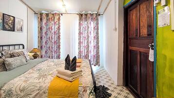 Um quarto com uma cama, almofadas, mesa de cabeceira com abajur, cortinas, uma porta e uma placa na parede.