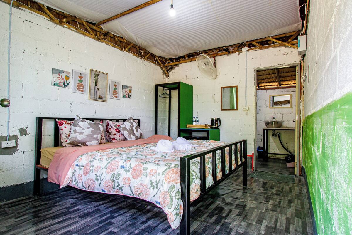 Una habitación con una cama, un armario verde, una pequeña cocina americana y un espejo.