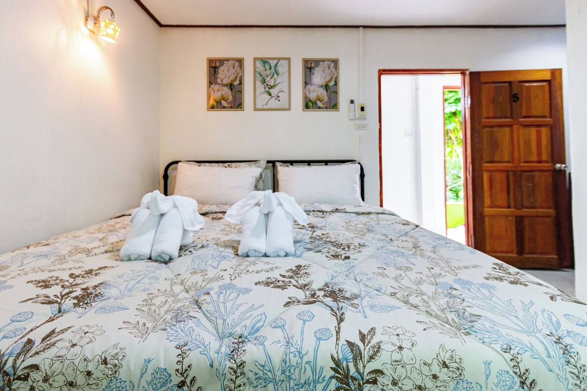 Un dormitorio con una cama, una puerta de madera y un muro con tres cuadros de flores.