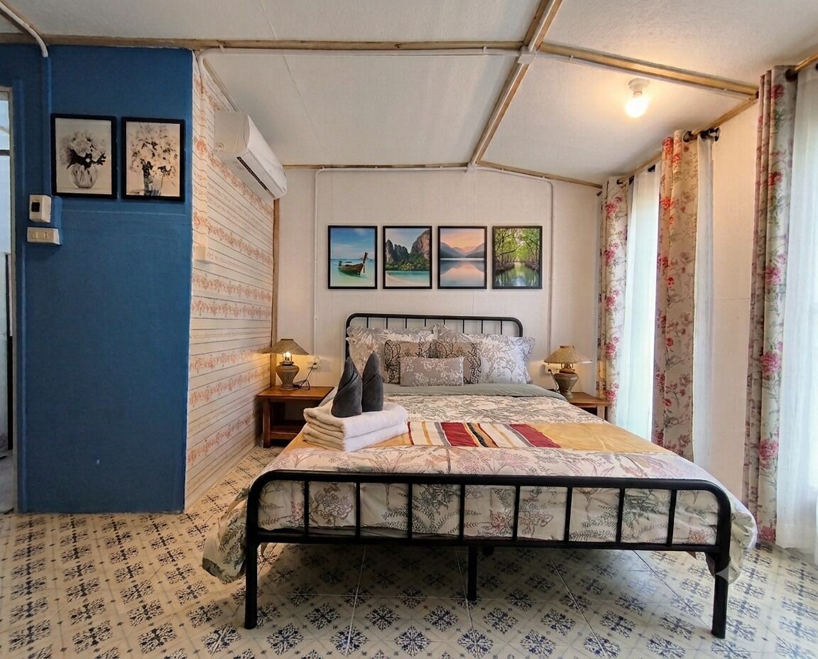 A single bed with a patterned bedspread, two bedside lamps, and a wall with framed pictures.