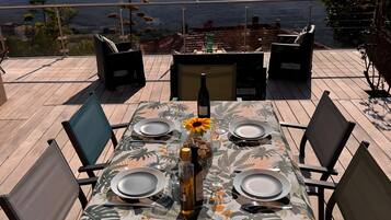 Une table à manger dressée pour six personnes, avec une nappe ornée d’un motif de feuilles tropicales, des chaises et une bouteille de vin.
