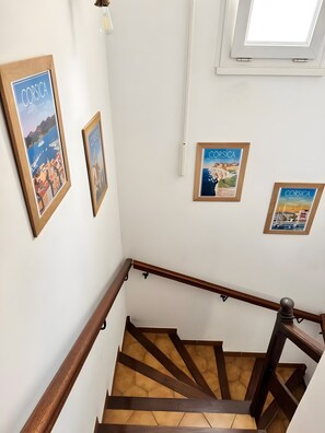 Una escalera con barandillas de madera, paredes blancas y carteles enmarcados de Córcega.