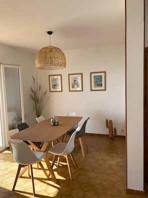 Un coin repas avec une table en bois, des chaises blanches, un luminaire suspendu, des tableaux encadrés au mur et une sculpture de cactus.