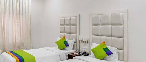 A hotel room with two beds, each with a headboard, white bedding, and colorful throw pillows.