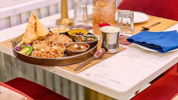 Una mesa de comedor con diversos platos, incluyendo arroz, curry y pan, junto con salsas y una botella de agua.