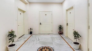 Un pasillo con suelo de mármol, puertas blancas y plantas en macetas.