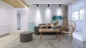 A modern living room with a grey sofa, wooden coffee table, and a round ottoman. A brick wall and a large window with curtains are visible. - Book and Bed - Lujiazui (Shanghai)