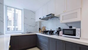 A modern kitchen with dark cabinets, a white countertop, a built-in microwave, and a window with a view of the outside. - Book and Bed - Lujiazui (Shanghai)