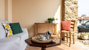 A cozy room with a white sofa, a wooden table with a tray, a chair, and a stone wall. - Cottage Zia Cherubina (Colle Brianza)