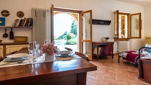 A dining area with a wooden table set for two, a window with a view of greenery, and a mirror on the wall. - Cottage Zia Cherubina (Colle Brianza)