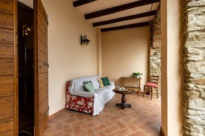 A cozy room with a wooden door, a sofa with floral upholstery, a small table, and a chair. - Cottage Zia Cherubina (Colle Brianza)