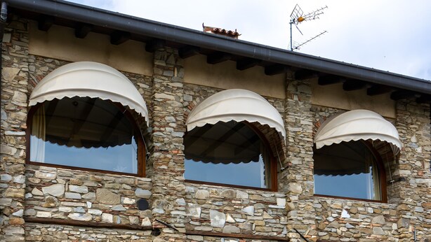 A stone building with multiple arched windows and a bench outside. - Cottage Zia Cherubina (Colle Brianza)
