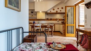 A cozy room with a bed, a dining table, and a kitchen area in the background. - Cottage Zia Cherubina (Colle Brianza)