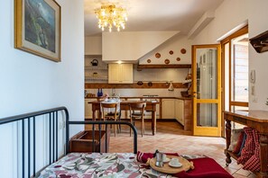 A cozy room with a bed, a dining table, and a kitchen area in the background. - Cottage Zia Cherubina (Colle Brianza)
