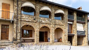 A stone building with multiple arches, balconies, and a gravel driveway with lavender plants. - Cottage Zia Cherubina (Colle Brianza)