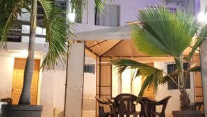 Un espace extérieur aménagé avec des tables et des chaises, entouré de palmiers en pot.