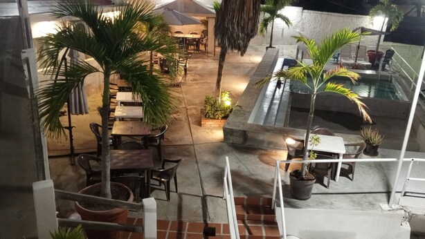 Un espace extérieur aménagé en terrasse, avec des tables et des chaises, entouré de plantes en pot et d’une petite piscine.