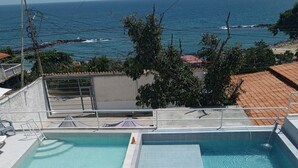 Une piscine avec vue sur l’océan, entourée d’une terrasse en béton et agrémentée d’un parasol blanc.