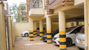 Autotalli, jossa on keltaisilla ja mustilla raidoilla varustetut pilarit, useita parkkeerattuja autoja ja tiilillä päällystetty lattia.