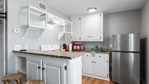 Una cocina con armarios blancos, un refrigerador de acero inoxidable, un microondas y taburetes de madera.