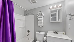 Un baño con bañera, inodoro, lavamanos y una pila de toallas en la pared.