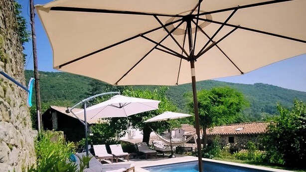 Un espace aménagé au bord de la piscine, avec des chaises longues et des parasols, entouré de verdure et délimité par un mur en pierre.