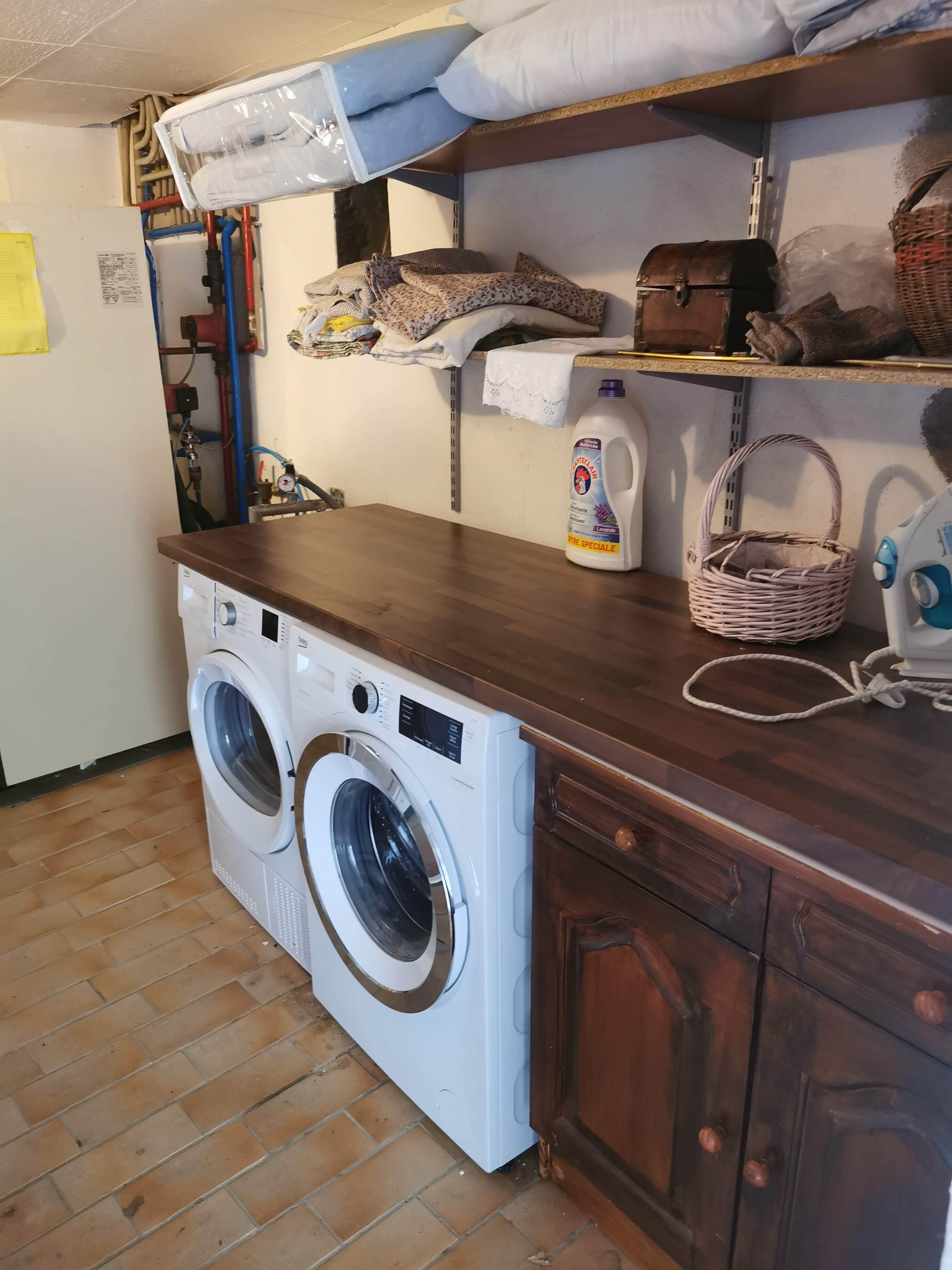A laundry room with a front-loading washing machine, wooden cabinets, a shelf with laundry supplies, and a tiled floor.