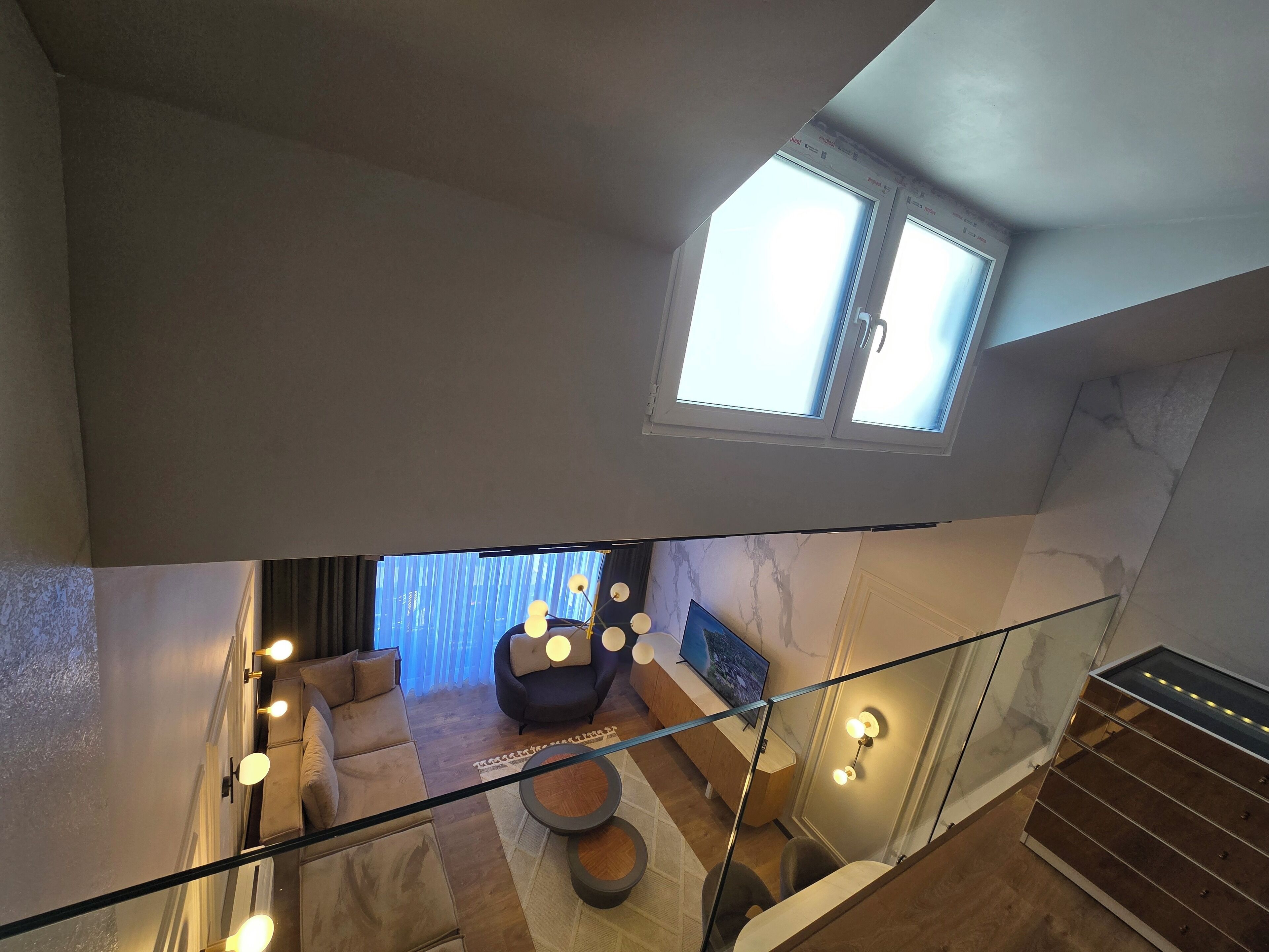 A high-ceilinged room with a large window, a glass railing, and a modern sofa set.