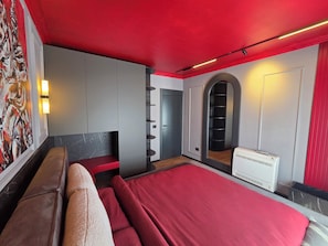 A modern bedroom with a red ceiling, a large bed, a bench, a wall-mounted shelf, and a radiator. - Apartments Lura (Peć)