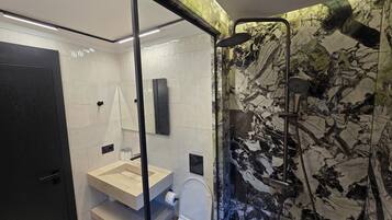 Ein modernes Badezimmer mit Duschwand aus Marmor, Toilette und Waschbecken mit Spiegel darüber.