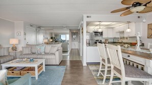 A spacious living room with a sofa, coffee table, and a dining area with chairs and a wooden table. - Thunder Island 161d 2 Bedroom Condo (Ocean City)