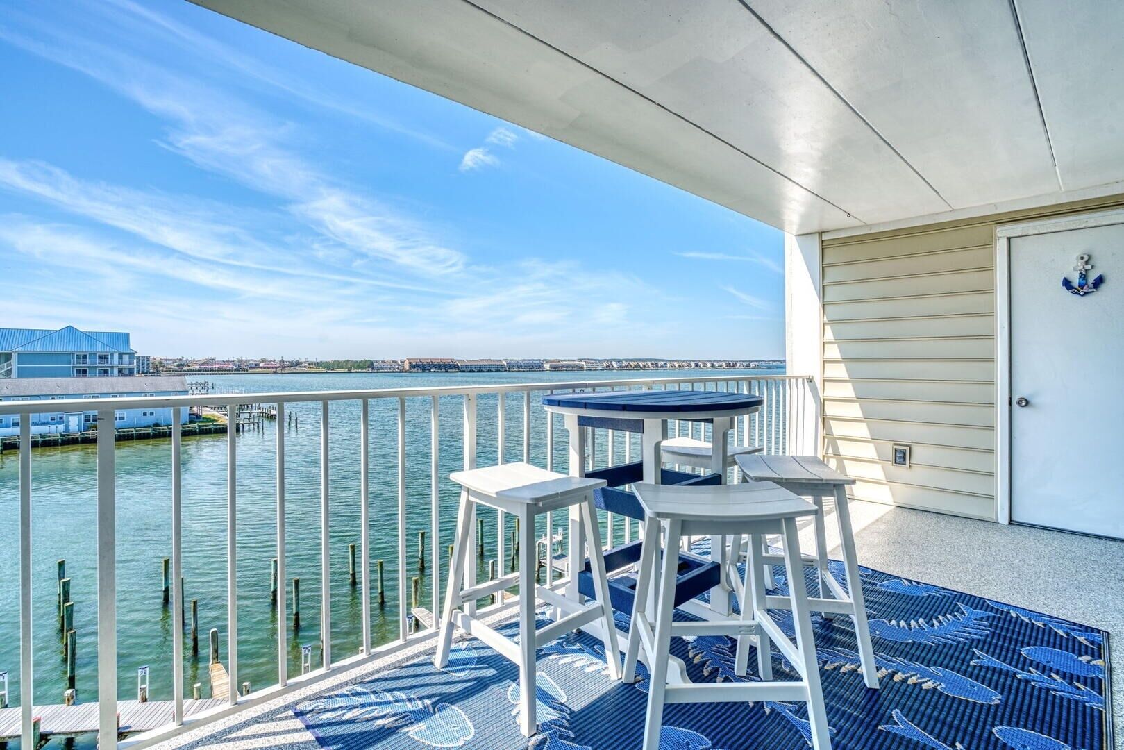 A balcony with a view of the water, a table, and chairs.